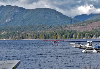 Two float planes and a dock, blue water and green mountain in background.