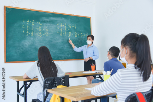 Asian teacher wearing facial mask while teaching students at school,all of student wearing facial mask and sitting far away from each other.