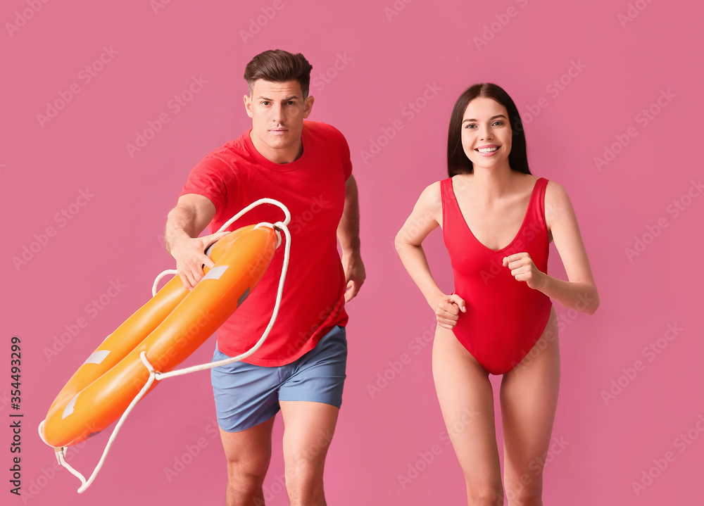 Running beach rescuers with lifebuoy on color background