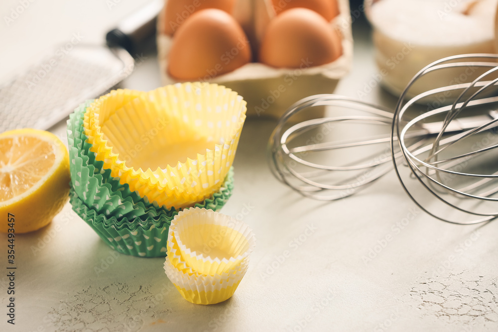 Muffin baking cups with products and utensils on light background