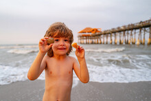 Cute, Happy Child Holding Shell At The Beach. Cute Little Boy At Tropical Beach Holding Sand Shell. Summer Travel And Beach Vacation.