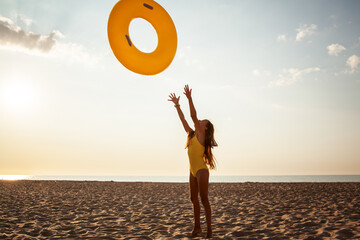 Happy girl throws an inflatable yellow ring to the sky. Lifestyle is the joy the summer vacation. The child dressed swimsuit.