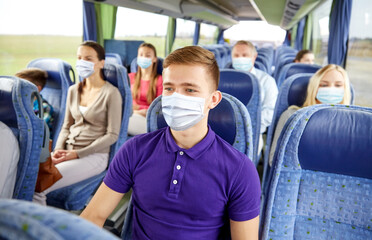 Poster - transport, tourism, road trip and people concept - young man wearing face protective medical mask for protection from virus disease sitting in travel bus or train