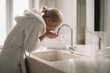 © JustLife - Beautiful woman enjoying in hotel. Young happy women in bathrobe wash her face.