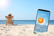 Young woman relaxing in deck chair on sandy beach and smartphone with open weather forecast app
