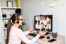Online Meeting, Remote Work. Young Business Woman With Glasses Using App On PC For Video Communication With Many People Together, She Has Headset For Talking Online With Employees. Back View