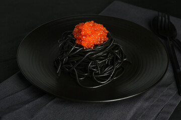 Squid ink black pasta with red caviar in a black plate on dark background. Black spaghetti with seafood. 