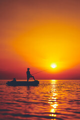 Silhouette of a fisherman fishing in sunset time on the open sea.