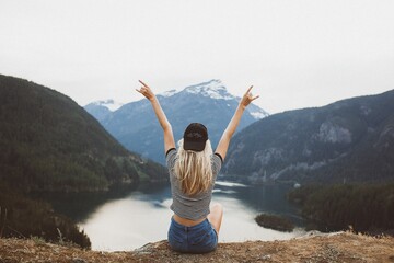 Canvas Print - Behind shot of a young blond girl sitting on the cliff enjoying the view of the mountains and lake