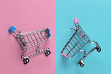 Two mini supermarket trolleys on blue pink pastel background. Shopping concept. Top view. Minimalism