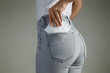Woman putting white menstrual feminine sanitary pad into jeans pocket on gray background
