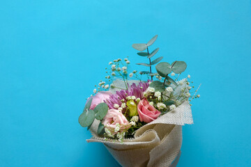 Hand flower bouquet consists of chrysanthemum, roses and green leaves on blue background.