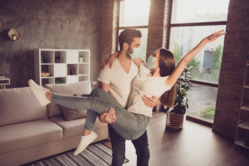 Canvas Print - Photo of young couple guy hold arms excited lady quarantine together stay home hugging happy have fun just married moved new flat wear facial medical mask living room evening sunset indoors