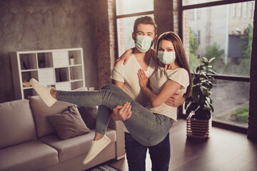 Canvas Print - Photo of funny young couple guy hold arms lady quarantine together stay home hugging happy have fun just married move new flat wear facial medical mask living room evening sunset indoors