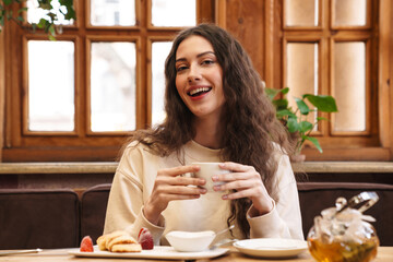 Canvas Print - Image of happy woman smiling and drinking tea while sitting in cafe