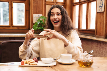 Wall Mural - Image of excited woman taking photo on cellphone while having breakfast