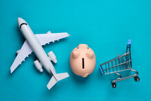 Shopping Still Life. Shopping Trolley, Piggy Bank Airplane Figurine On A Blue Background. Top View