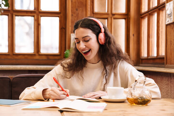 Canvas Print - Image of joyful student woman using headphones while doing homework