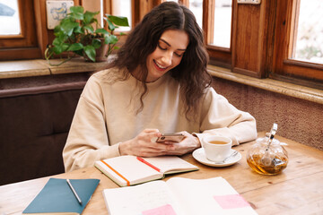 Canvas Print - Image of woman doing homework and using cellphone while drinking tea