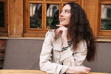 Canvas Print - Image of woman looking aside and smiling while sitting in street cafe