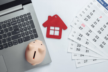 Wall Mural - Paying rents for housing or searching for housing online. Laptop with piggy bank, house figurine with a monthly calendar. Top view