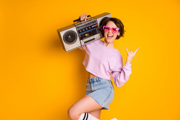 Poster - Yeah rock rules. Positive cheerful girl hold boom box listen youth music show finger horns symbol scream rejoice wear pink sweater jeans isolated over bright shine color background