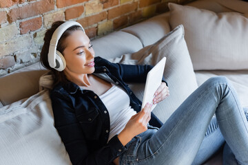 cheerful girl in wireless headphones listening music and using digital tablet