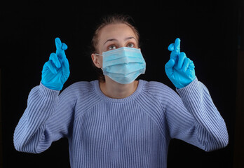 I wish! Woman in medical face mask and gloves crossed her fingers on a black background