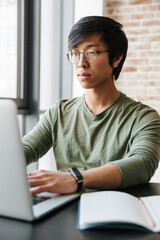 Sticker - Image of handsome young asian man using laptop in apartment