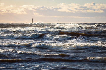 Windy late evening sunset view to Baltic sea lighthouse with large storm waves.