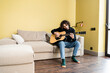 © LIGHTFIELD STUDIOS - Curly man playing acoustic guitar while sitting on couch at home