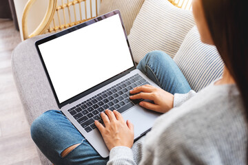 Top view mockup image of a woman working and typing on laptop computer with blank screen while sitting on a sofa at home