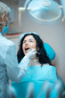© goami - beautiful brunette curly female dentist treat patient in modern clinic