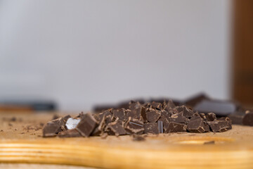 Selective focus close up shot of chattered dark chocolate pieces on wooden plate.