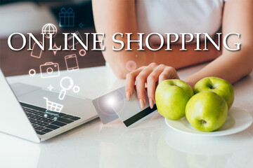 Wall Mural - cropped view of woman with laptop holding credit cards on kitchen with apples during self isolation with online shopping lettering and signs