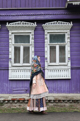 Russian girl in Pavlovo Posad shawl. Wooden traditional rural house with ornamental carved windows, frames in Ivanovo city, Russia. Russian folk style in architecture, architectural fashion. Landmark