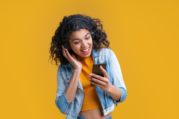 Wall Mural - Cute smiling dark skinned girl in wireless headphones enjoying listening to music