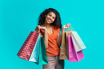 Wall Mural - Cute dark skinned girl with perfect smile posing with piles of shopping bags isolated over bright blue background