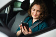 © scharfsinn86 - Woman driver sitting in car and looking at smartphone screen