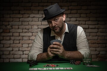 Poker player with cards and playing chips a the poker table -  poker in a dark back room with a brick wall