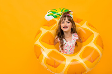 Beautiful little girl in swinsuit holds a rubber ring and smiles isolated on yellow and orange background