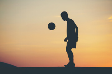 Wall Mural - Silhouette of a man playing soccer in golden hour, sunset.