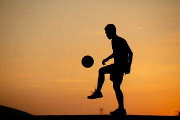 Wall Mural - Silhouette of a man playing soccer in golden hour, sunset.