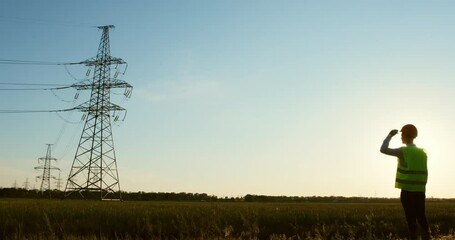 Wall Mural - a man in a protective helmet and a green signal vest looks at the power line.