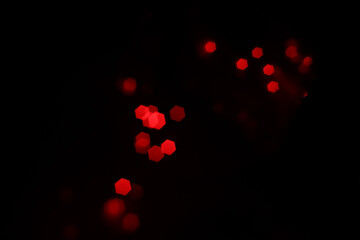 Red hexagonal bokeh lights on dark background from unfocused macro, created with red fairy lights and a vintage lens. 