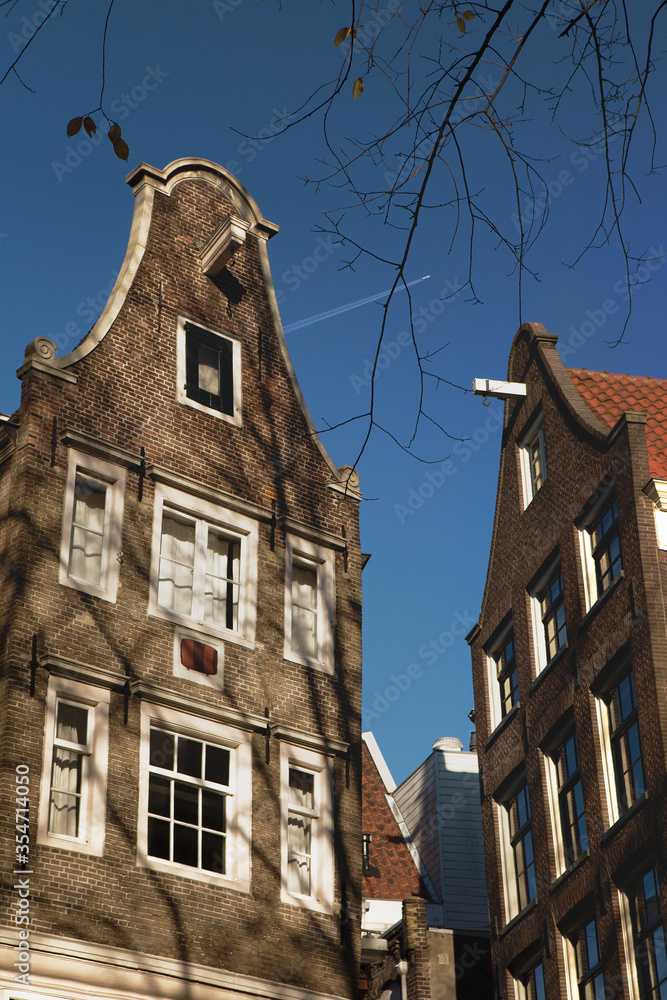 Detail of the typical duch inclined houses in the center of Amsterdam, the most touristic city in the Netherlands. - obrazy, fototapety, plakaty 