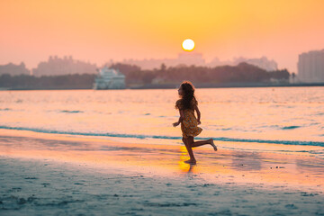 Wall Mural - Adorable happy little girl on white beach at sunset.