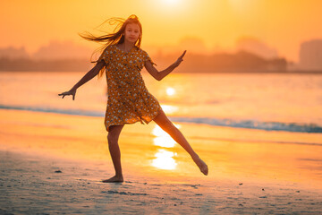 Wall Mural - Adorable happy little girl on white beach at sunset.