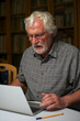 © Sahara Frost - Portrait of a white bearded senior man with grey shirt looking at a laptop, notebook screen.