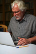 © Sahara Frost - Portrait of a white bearded senior man with grey shirt looking at a laptop, notebook screen.